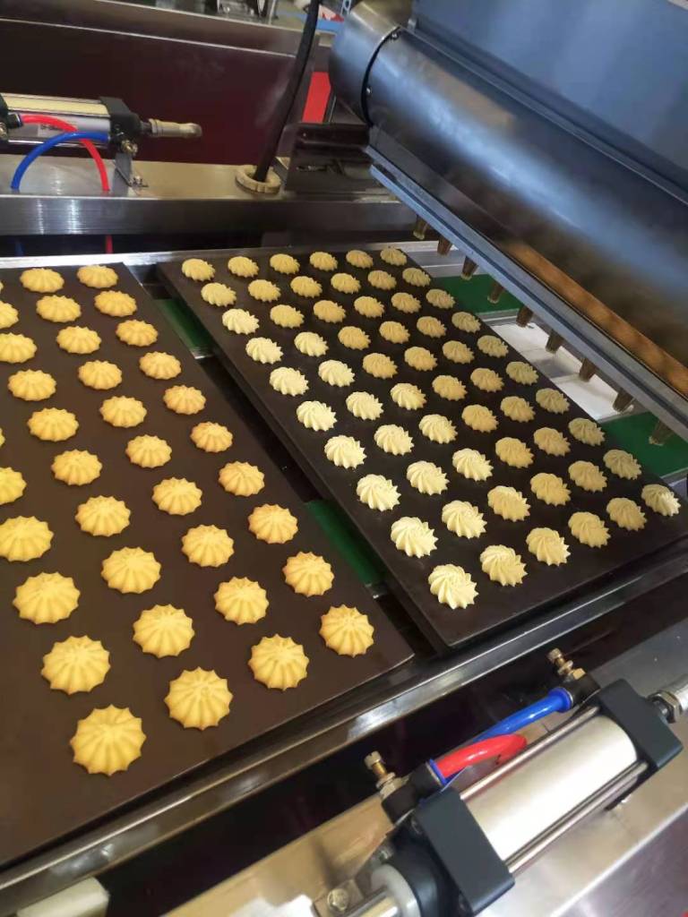Trays of dough formed into decorative shapes by a cookie-making machine.